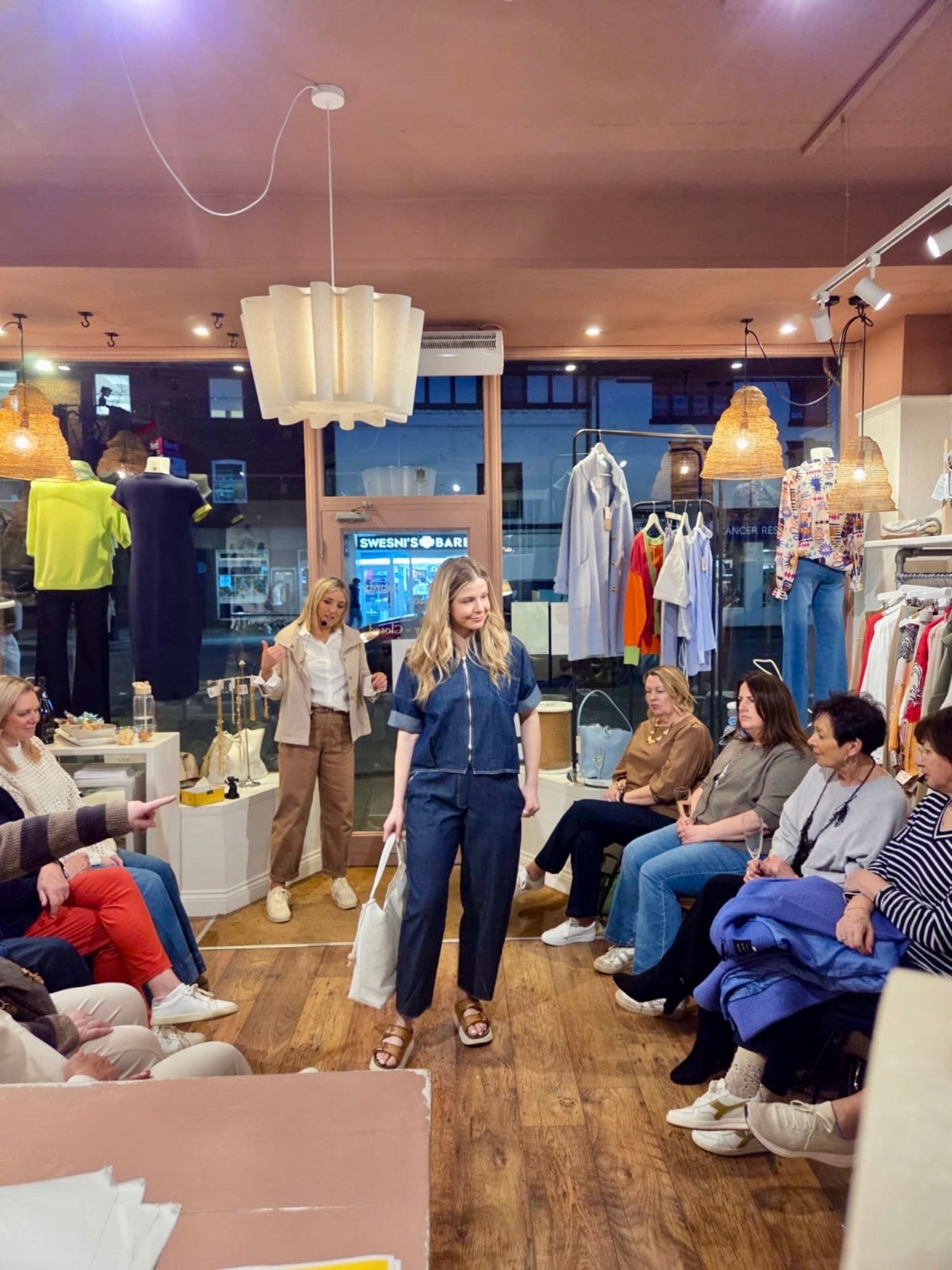 Woman in a blue outfit walking through a clothing store with an audience watching.
